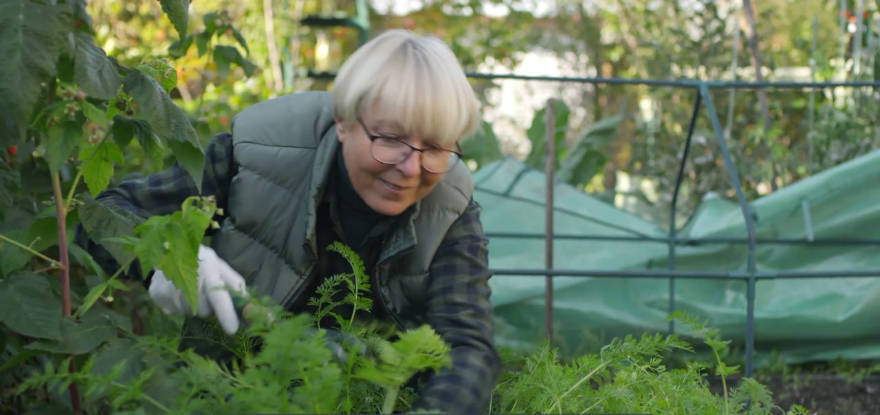 A woman kneeling in her vegetable garden, smiling