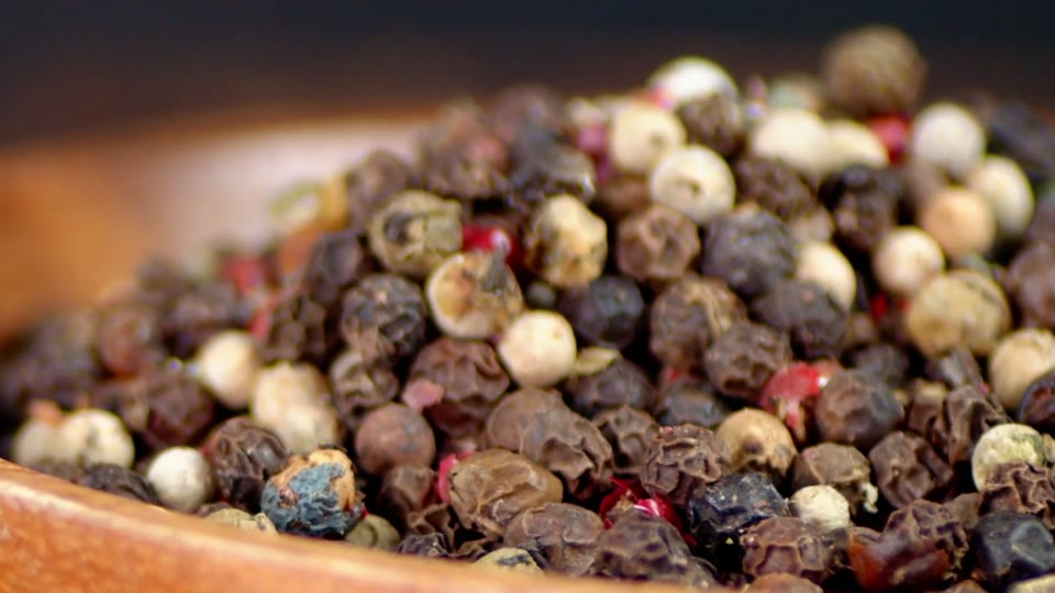 A wooden bowl of black peppercorns